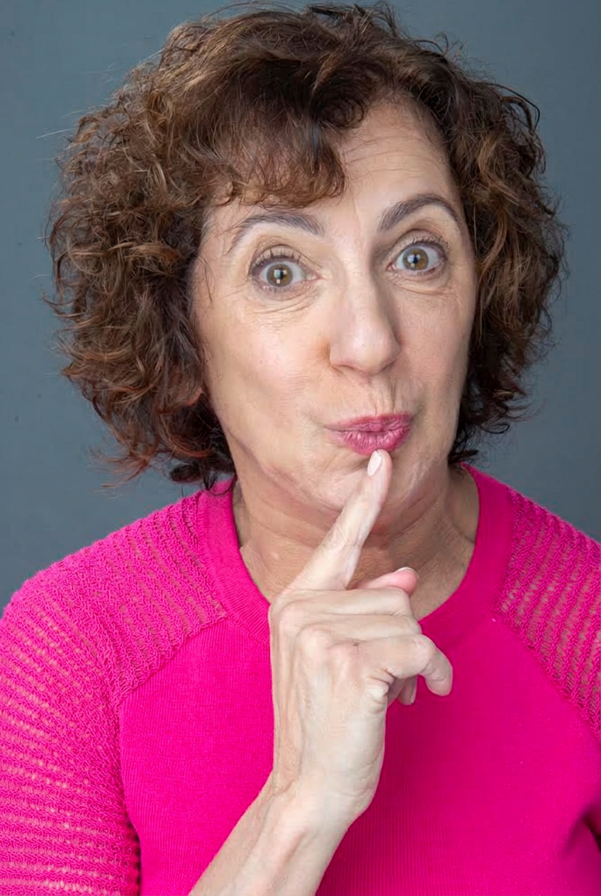 Nancy Levine headshot in a pink sweater with finger to lips